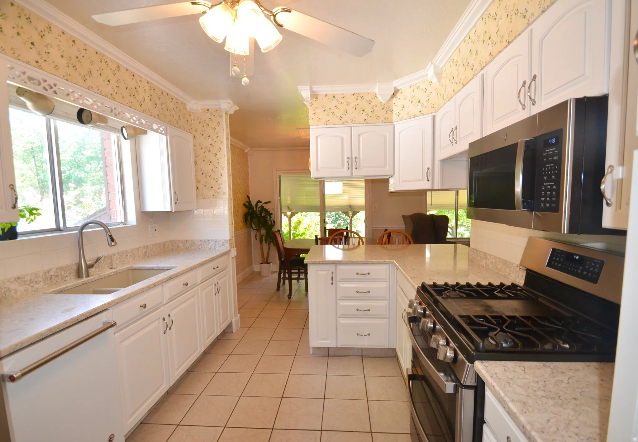 Galley kitchen featuring white cabinetry, light-toned countertops, tile flooring, and stainless steel appliances including a gas range and microwave