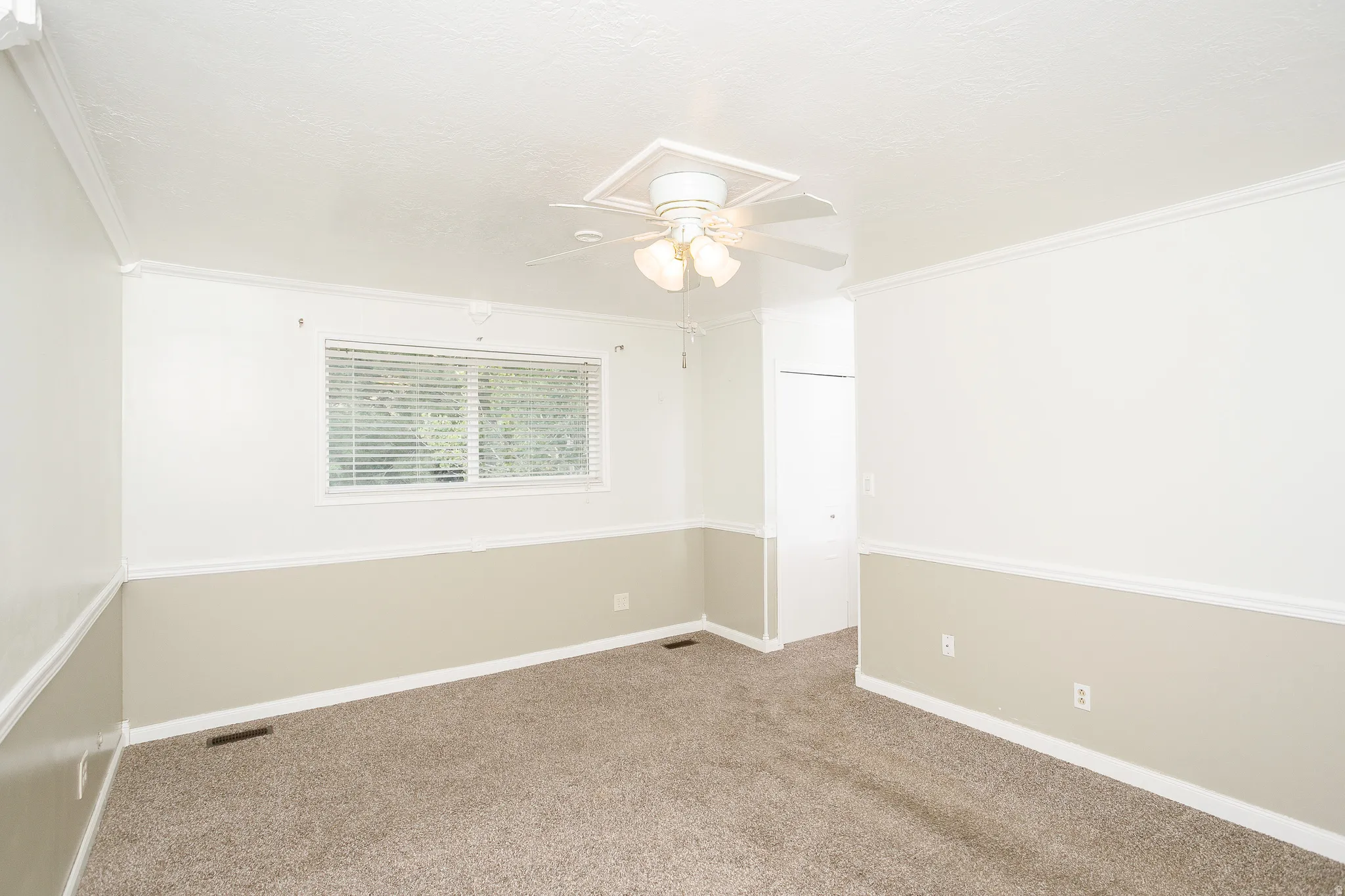 Carpeted interior space featuring a ceiling fan with light fixture, window with blinds, and white trim molding