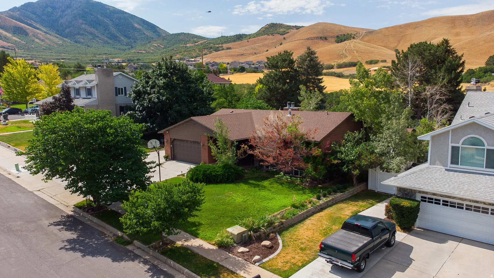 Single-story residence featuring a two-car garage, mature front yard landscaping with vibrant green lawn, and a paved driveway