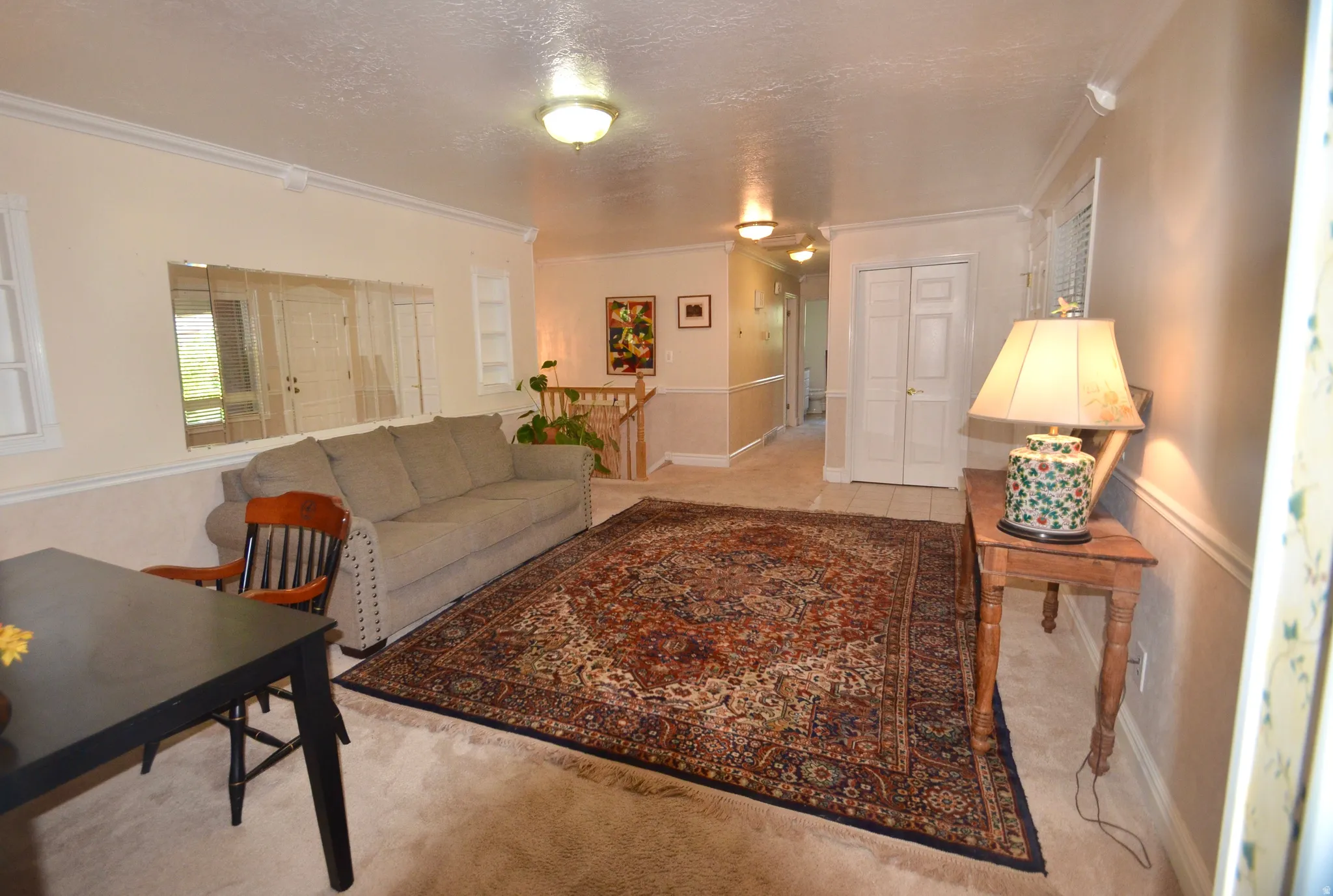 Carpeted living area featuring a large area rug, crown molding, and wall sconces