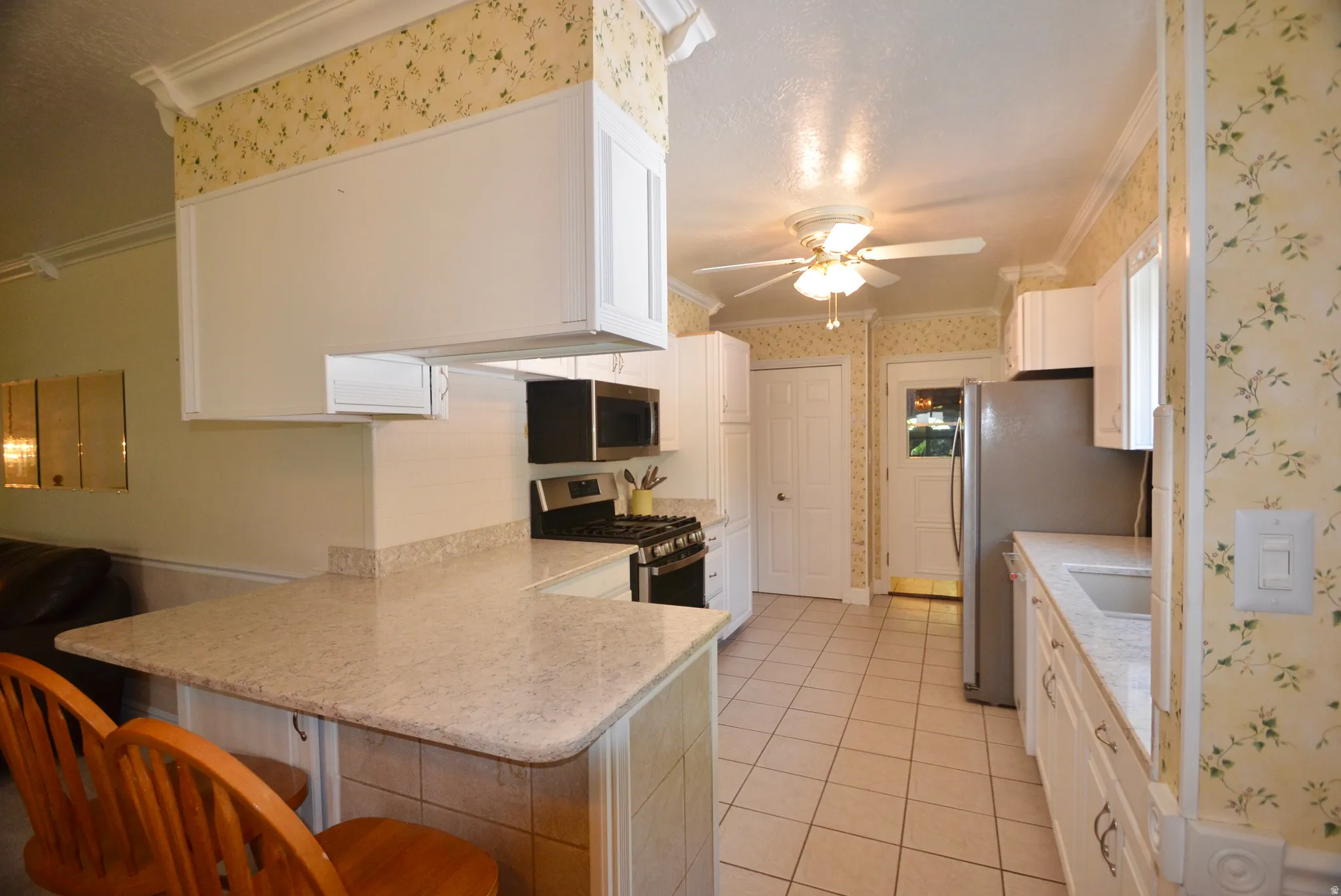 Kitchen featuring white cabinetry, light-toned countertops, a built-in microwave, a gas range, and tile flooring