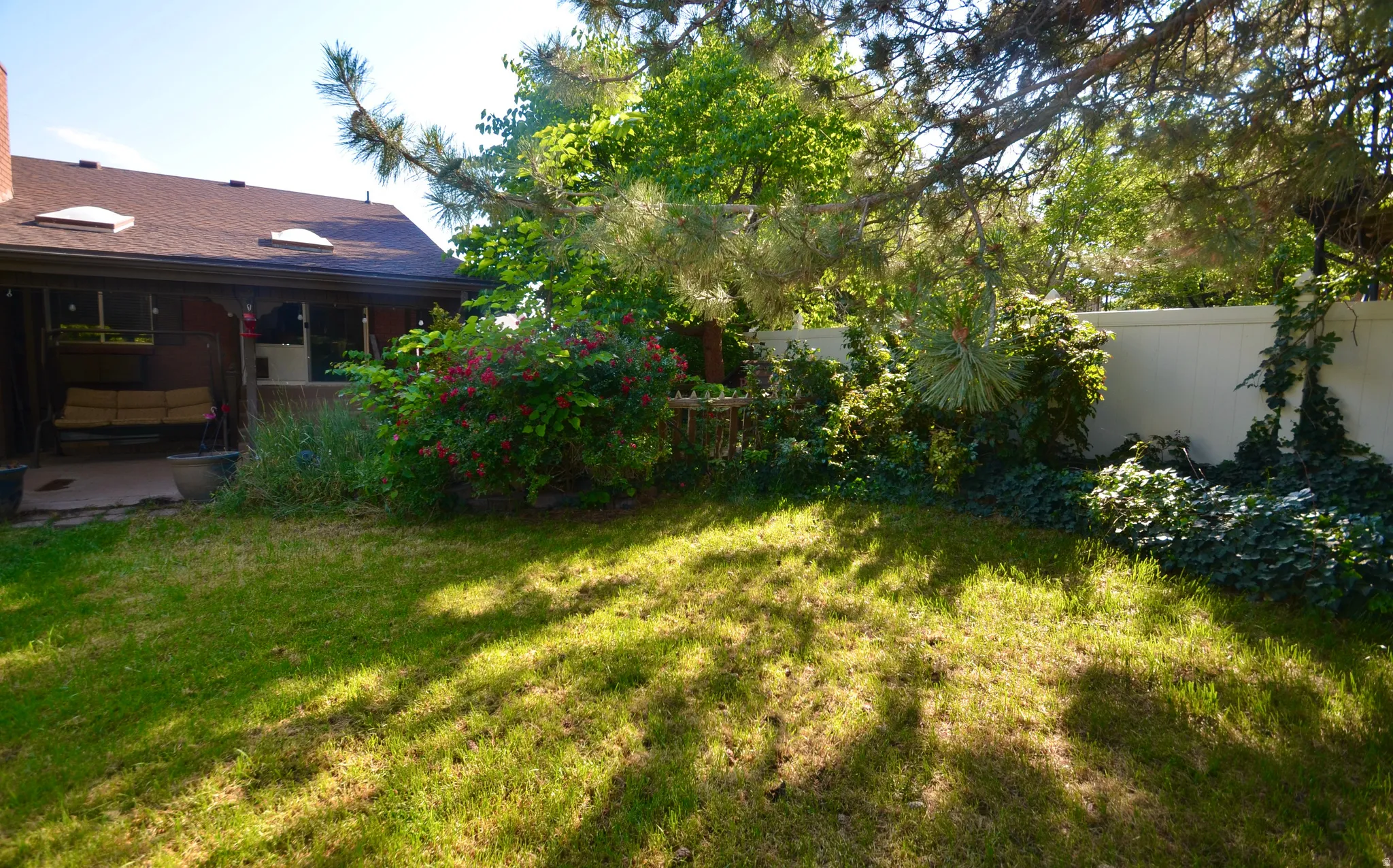 Spacious lawn area featuring mature trees, a covered patio, and perimeter fencing