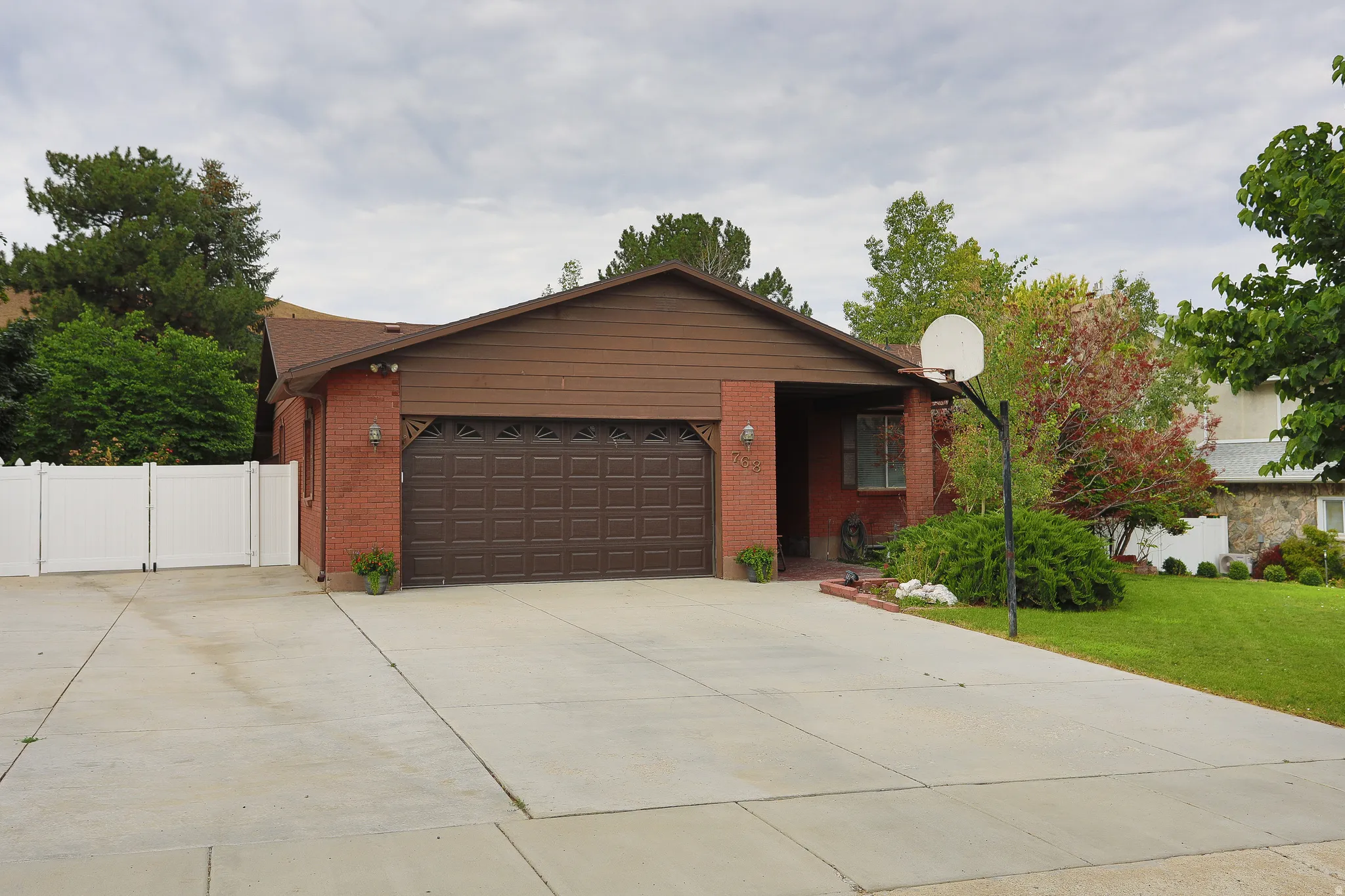 Brick exterior with a brown garage door, expansive concrete driveway, and a white privacy fence