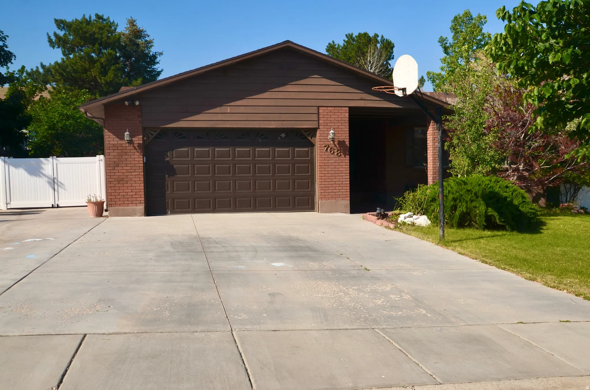 Brick facade residence featuring a two-car garage with a paneled door, a paved driveway, and mature landscaping