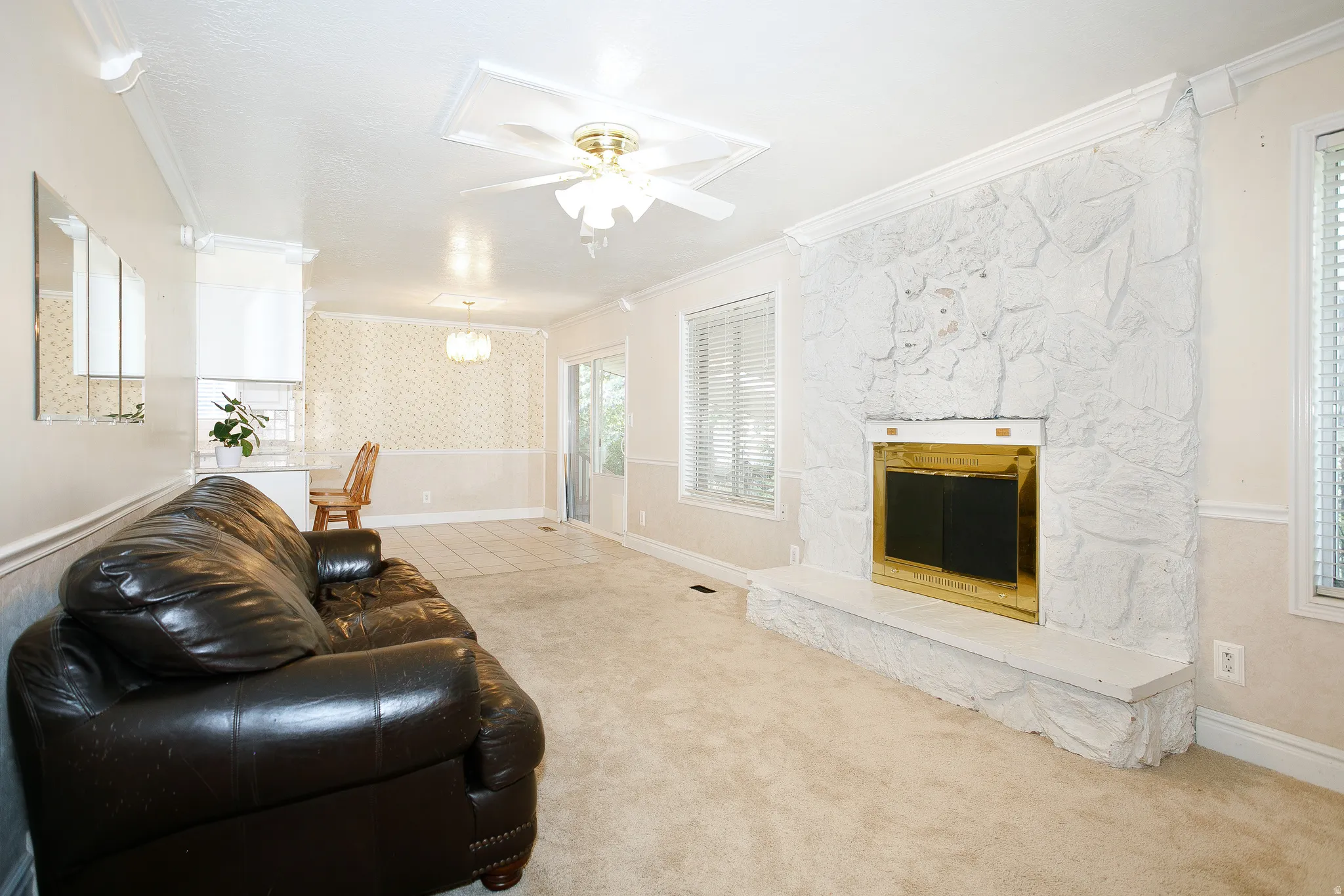 Living area featuring a textured stone fireplace with a brass firebox, ceiling fan with light fixture, and crown molding