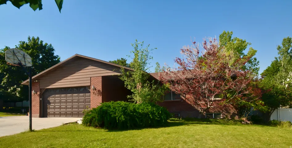 Brick-front residence featuring a two-car garage with a paneled door, partial siding, a pitched roofline, and a mature front yard with established landscaping
