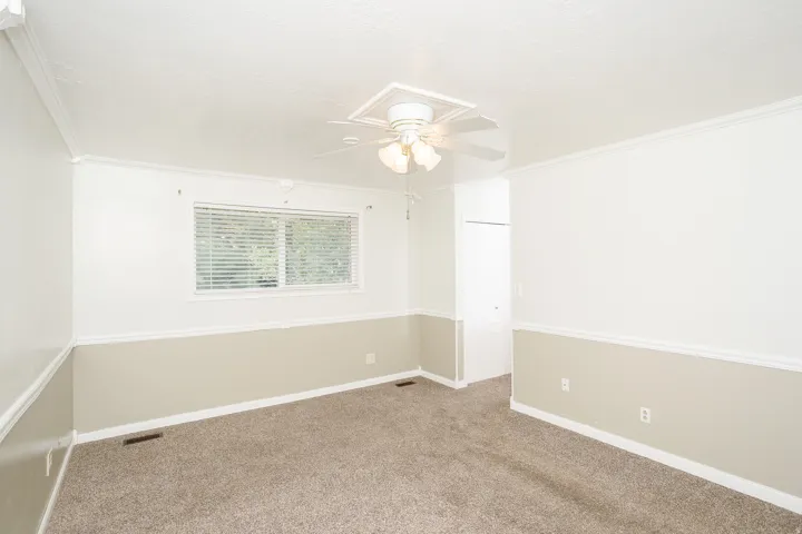 Carpeted interior space featuring a ceiling fan with light fixture, window with blinds, and white trim molding