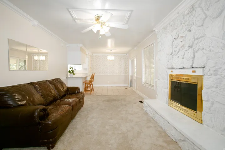 Living room featuring a prominent white stone fireplace with a gold-toned insert, crown molding, and a ceiling fan