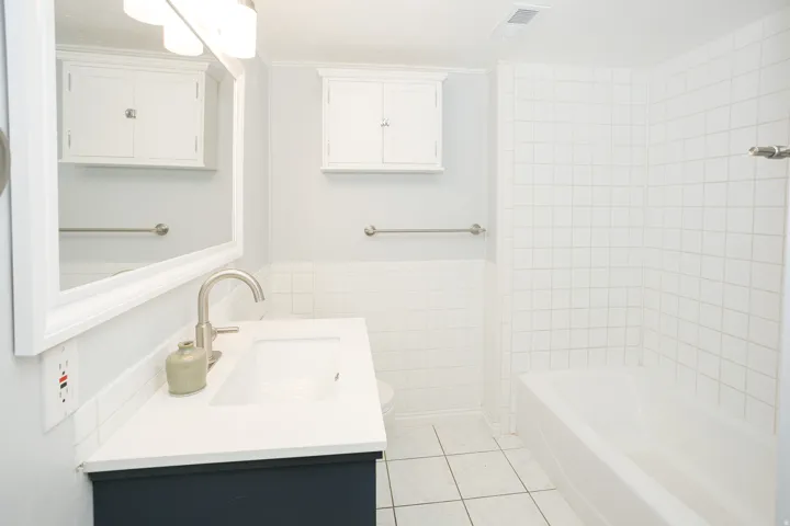 Bathroom featuring a white tile shower surround, a built-in bathtub, and a dark blue vanity with a white countertop and undermount sink
