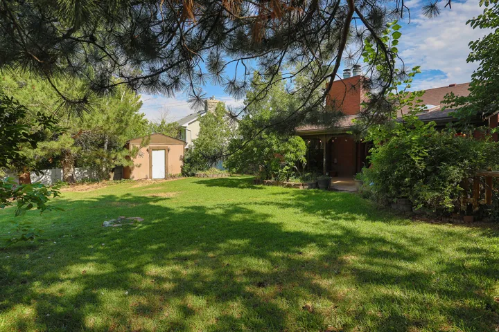 Expansive backyard featuring a manicured lawn, established trees, and a functional storage shed