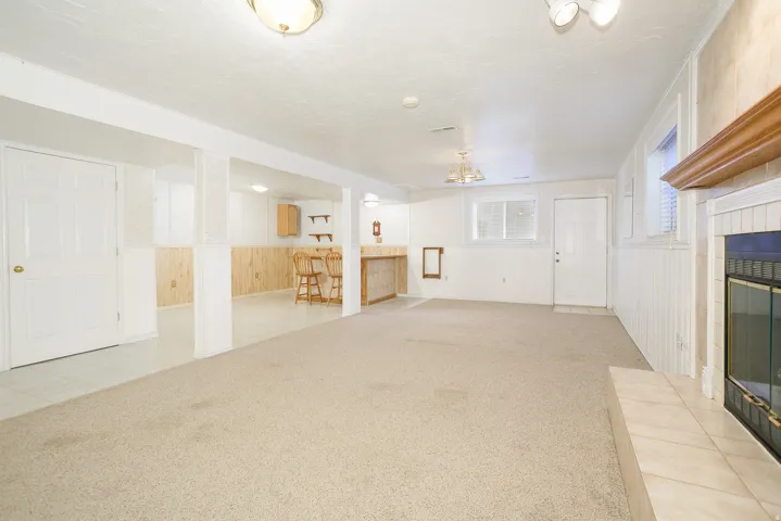 Carpeted lower level with a built-in wet bar, recessed lighting, and a fireplace featuring a tile hearth and wood mantel