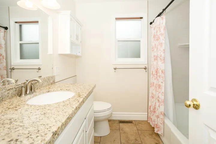 Bathroom featuring a granite-finish vanity countertop with an undermount sink, brushed nickel faucet, white cabinetry, tiled flooring, and a window