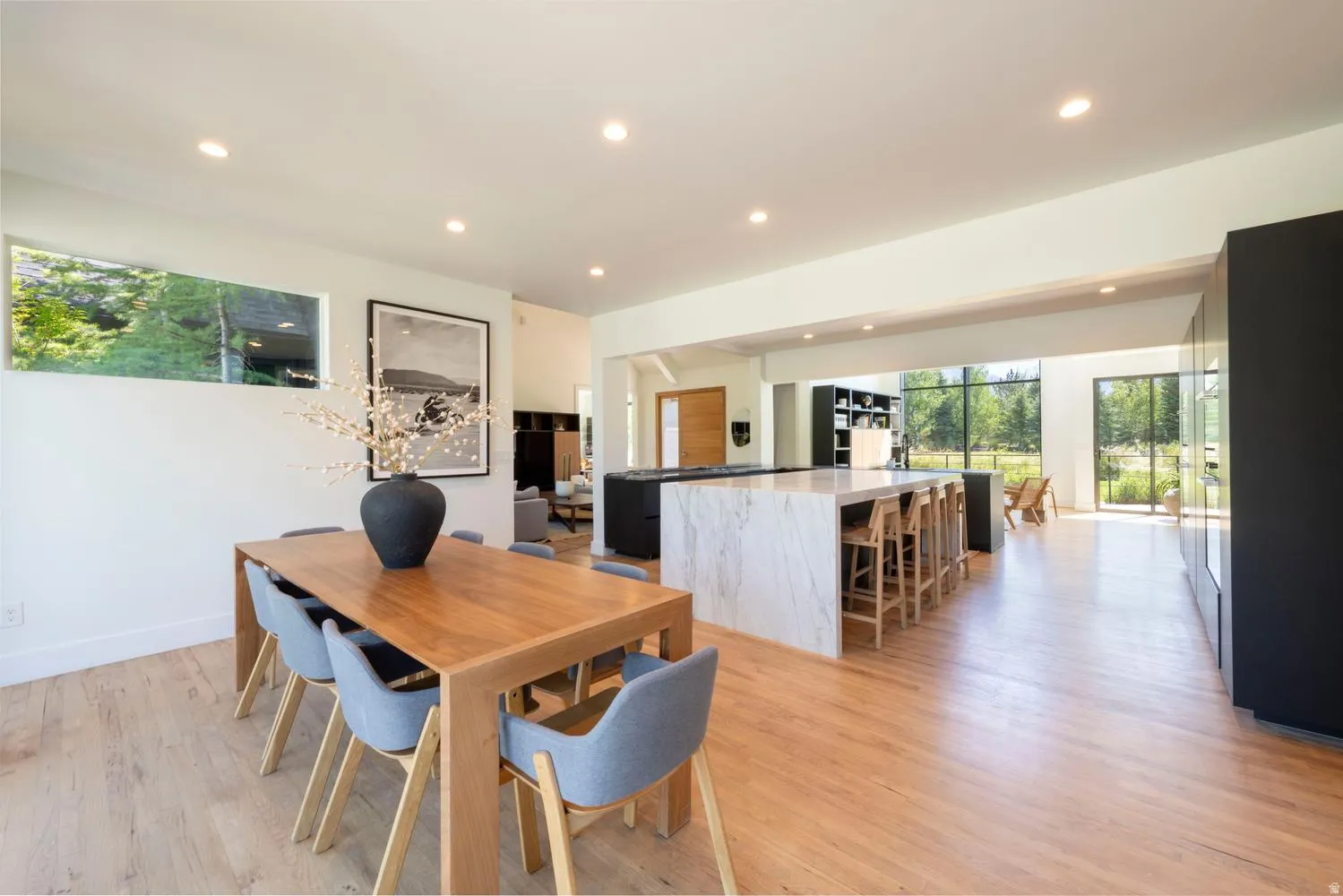 Spacious open-concept living area featuring light wood-finish flooring, a large white kitchen island with seating, beautiful cabinetry and extensive floor-to-ceiling windows