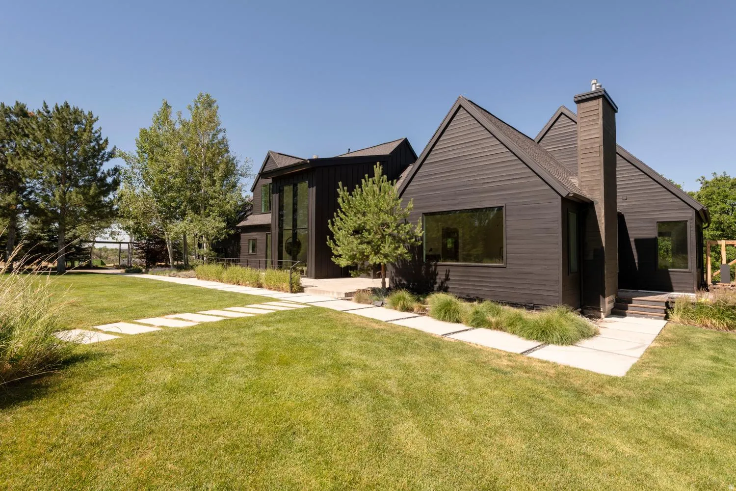 Contemporary exterior featuring dark wood siding, a prominent chimney, and multiple large windows