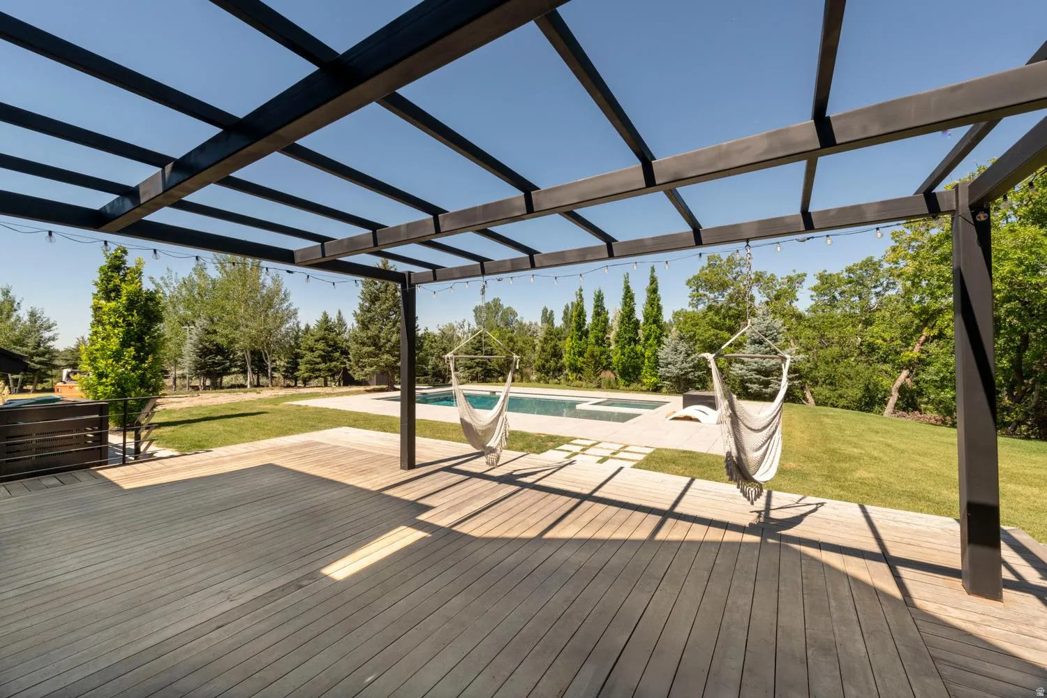 Expansive outdoor living area featuring a wood-finish deck, a modern pergola, and string lighting