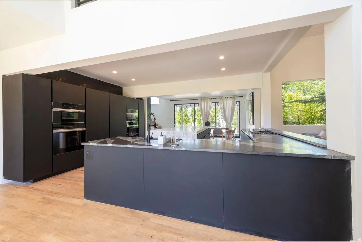 Modern remodeled kitchen featuring dark cabinetry, integrated double ovens, and wood-finish flooring
