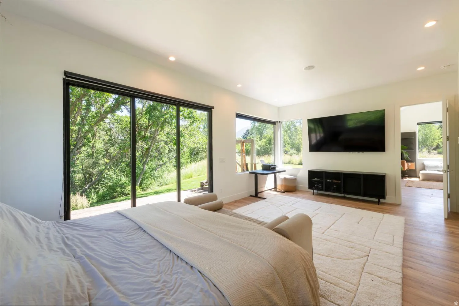 Expansive sliding glass doors, wood-finish flooring, recessed lighting, white walls, and a large window in primary suite
