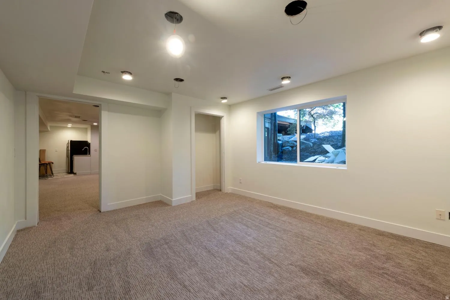 Spacious room featuring neutral carpeting, a large white-framed above grade window, recessed lighting, and crisp white baseboards