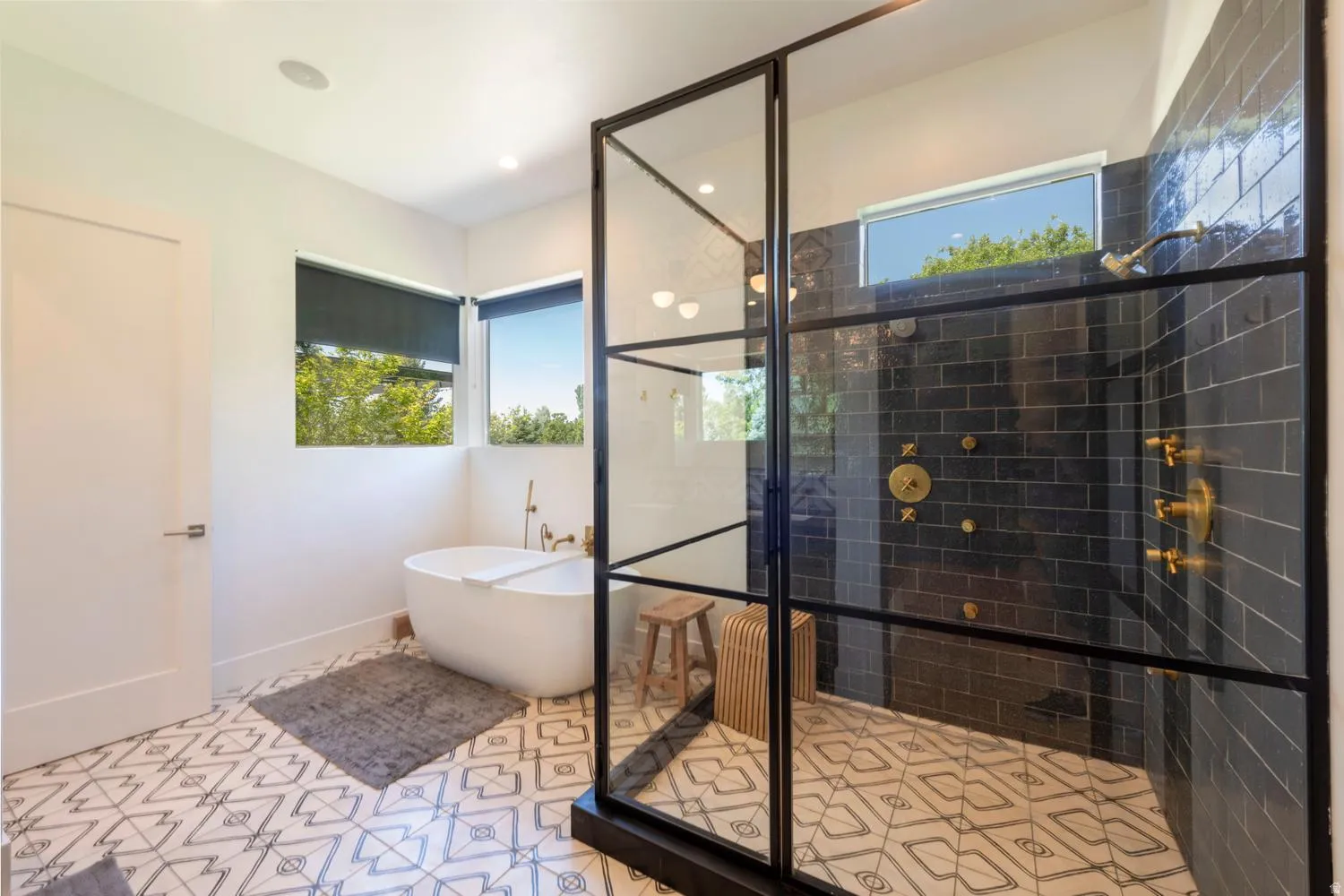 Primary suite bathroom featuring a freestanding tub with brass fixtures, a large walk-in shower with black subway tile, and a black-framed glass enclosure