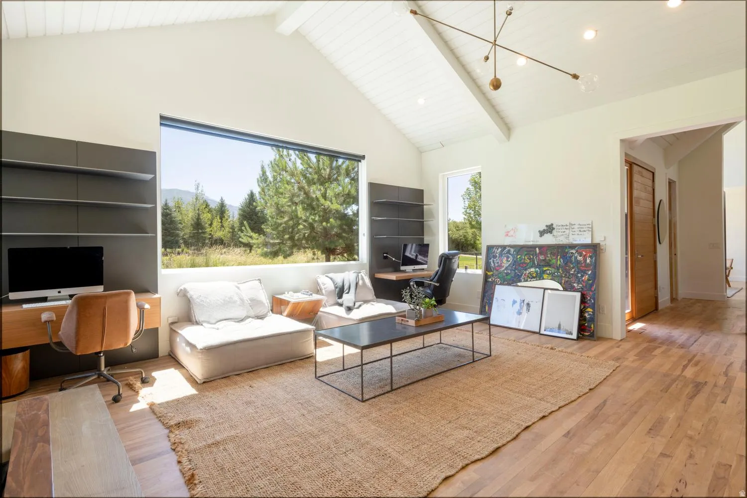 Spacious office/den off primary suite featuring a vaulted ceiling with exposed beams, large picture windows, wood-finish flooring, built-in shelving, and a contemporary chandelier