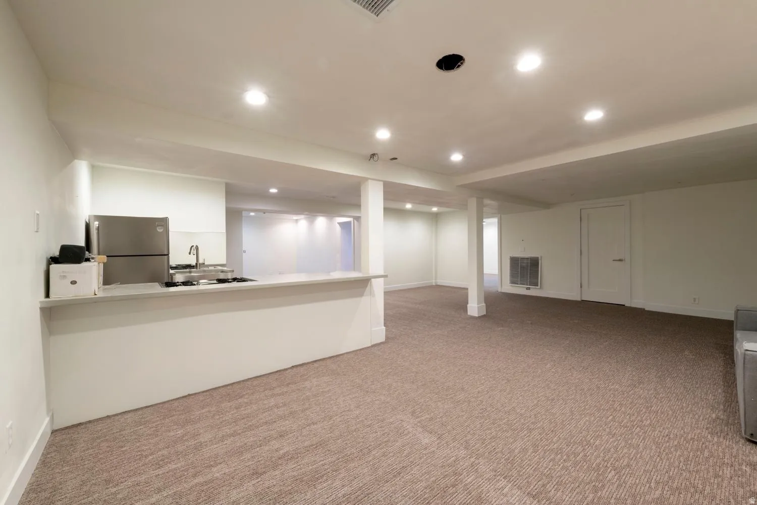 Spacious open-concept lower level featuring recessed lighting, light-toned carpeting, and a kitchen area with a stainless steel refrigerator and sink