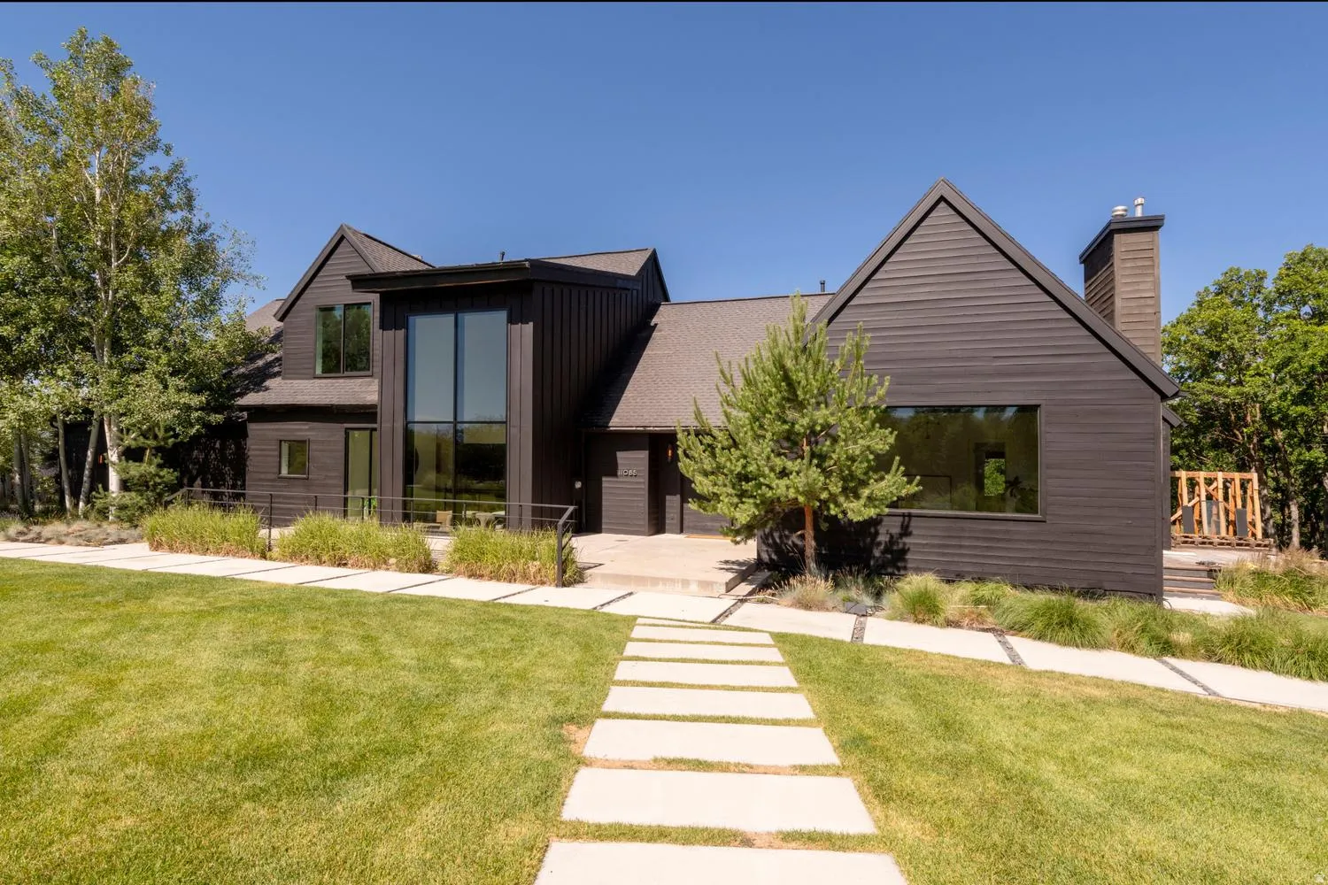 Front of home with a prominent floor-to-ceiling window, a contrasting light-toned pathway, a gabled roofline, and an integrated chimney