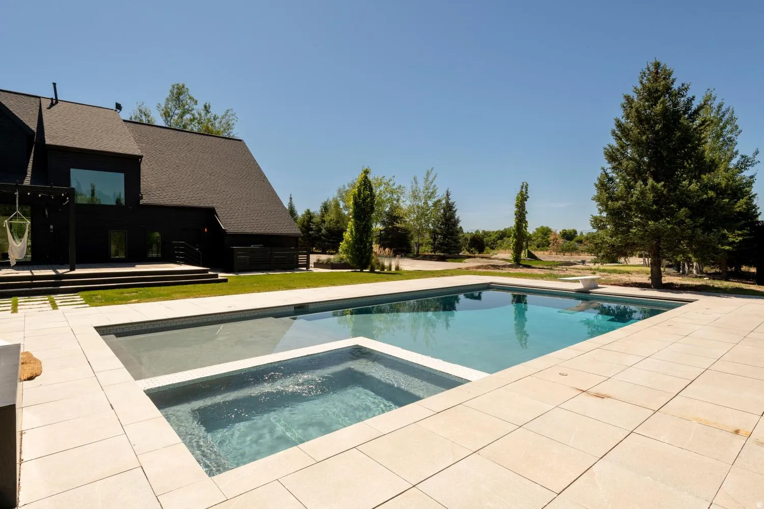 Expansive outdoor living area featuring a rectangular pool with an integrated spa, surrounded by large decking