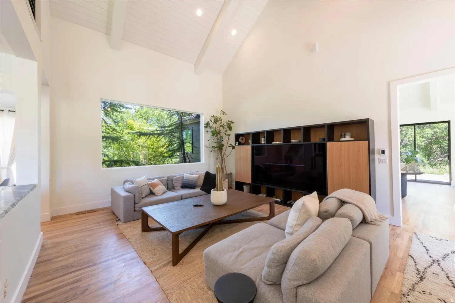 Expansive living area featuring soaring vaulted ceilings with exposed beams, recessed lighting, and wood-finish flooring