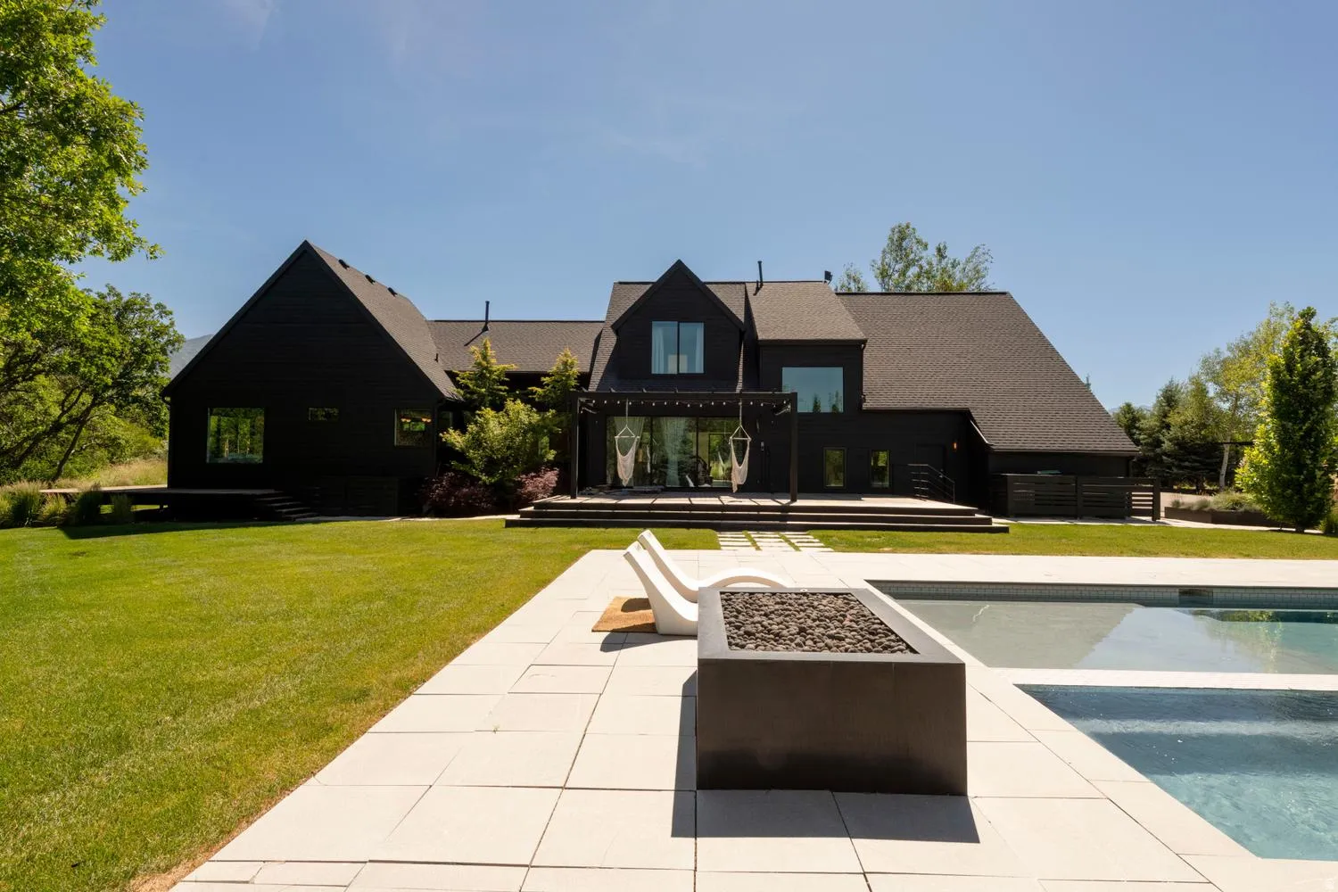 Contemporary black exterior featuring multiple gables, swimming pool and fire pit