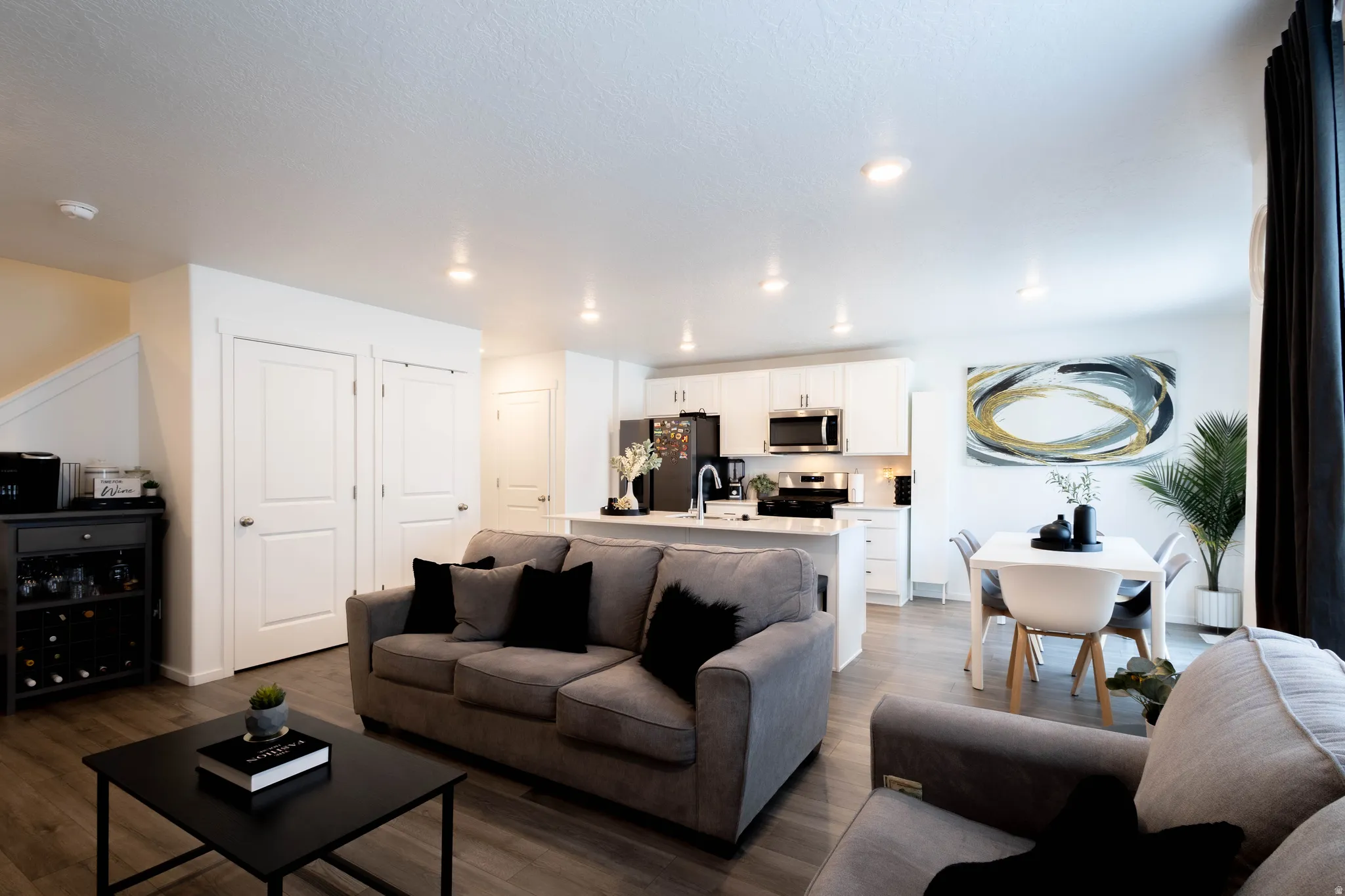 Open-concept living area featuring wood-finish flooring, recessed lighting, and a white kitchen with stainless steel appliances