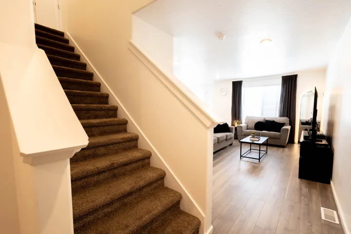 Carpeted staircase with white balustrade, wood-finish flooring, white walls, and a recessed ceiling light