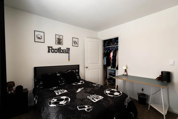 White walls and textured carpeting define this bedroom, featuring a built-in closet with shelving and hanging rods