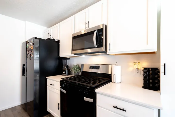 Kitchen featuring white cabinetry, stainless steel microwave, black gas range, solid surface countertops, and wood-finish flooring