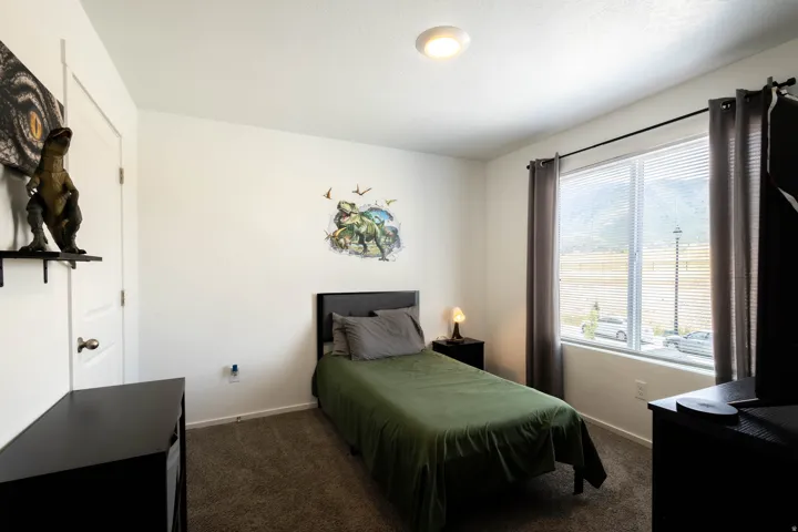 Bedroom featuring plush carpeting and a large window with horizontal blinds