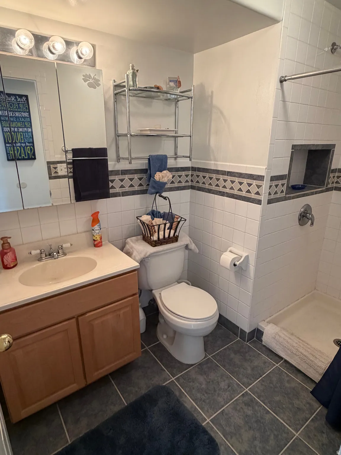 Bathroom featuring a wood-finish vanity with an integrated sink, a medicine cabinet with vanity lighting, and a tiled shower with a built-in niche