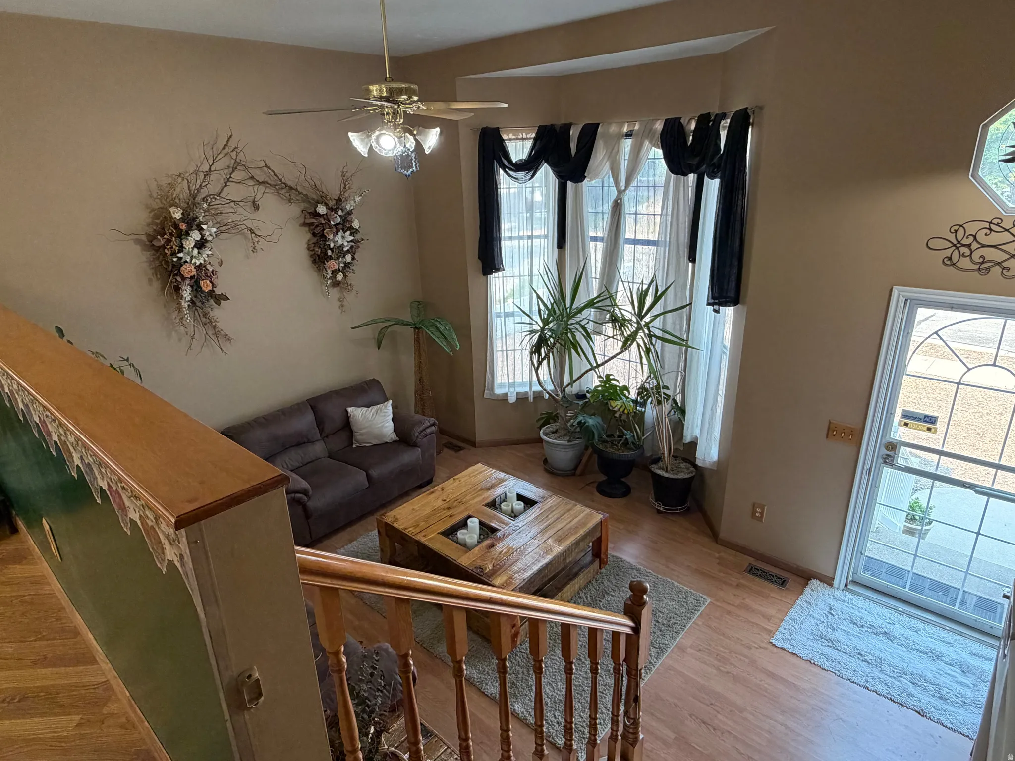 Vaulted ceiling living area featuring wood-finish flooring, bay windows, and a ceiling fan