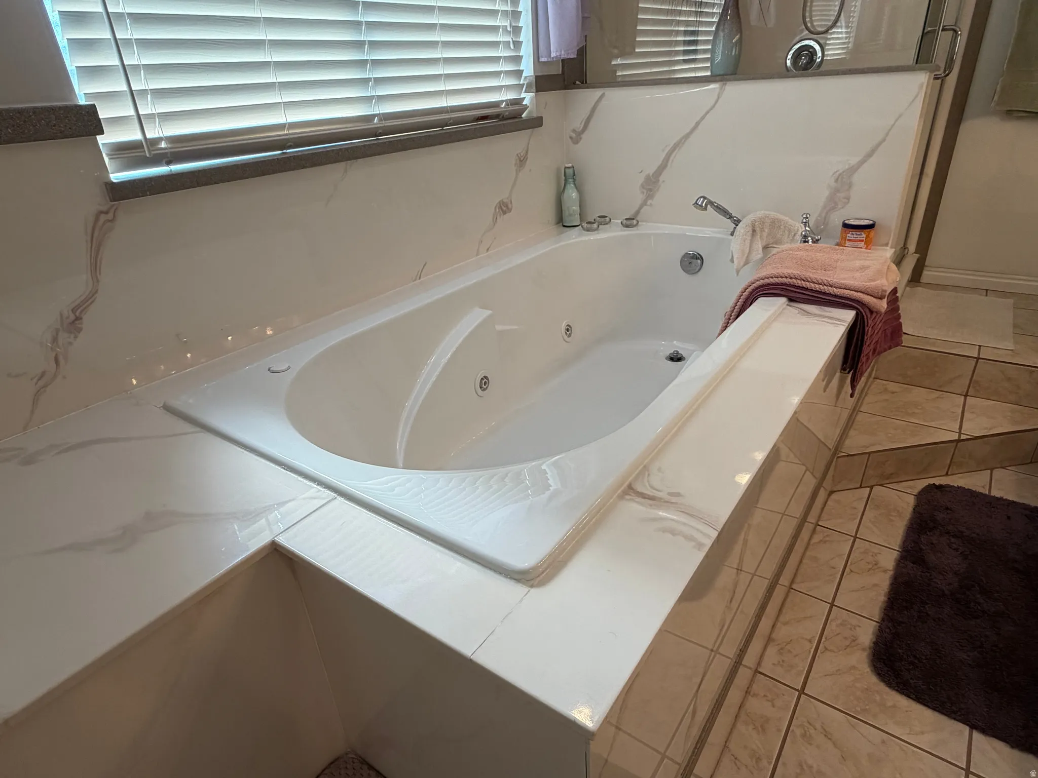 Integrated soaking tub featuring a tiled surround with a marble-effect finish, chrome fixtures, and a tiled floor
