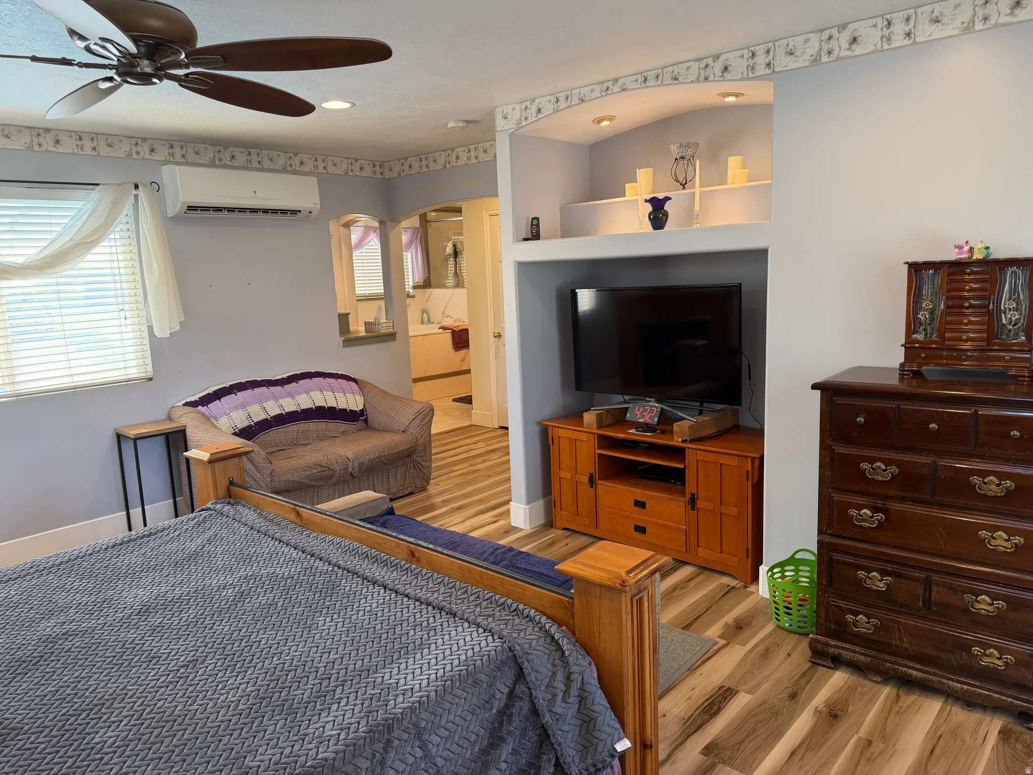 Bedroom featuring wood-finish flooring, a ceiling fan, a mini-split air conditioning unit, and a built-in entertainment niche with accent lighting