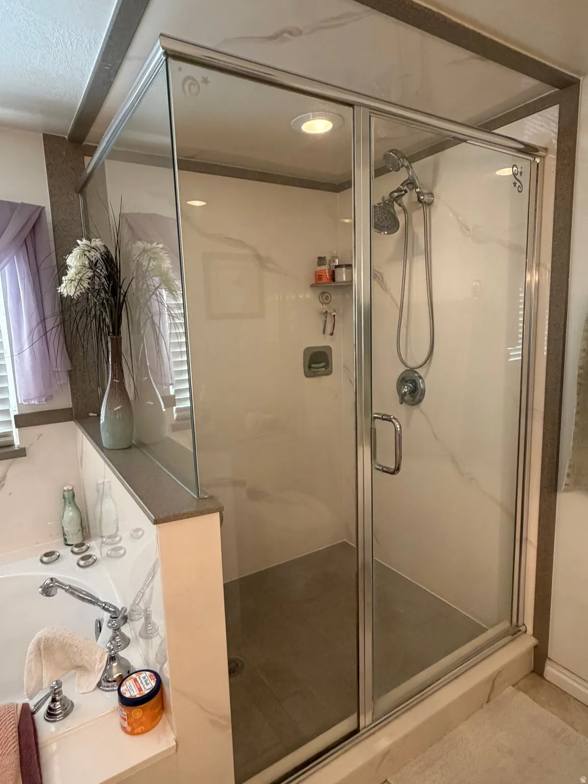 Glass-enclosed shower featuring a sliding door, dual shower heads, and an integrated shelf