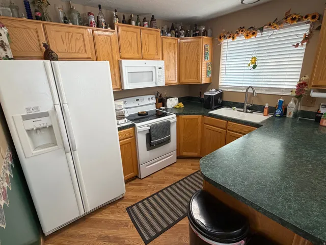 Kitchen featuring wood-finish flooring, oak cabinetry, white appliances, and a double-basin sink