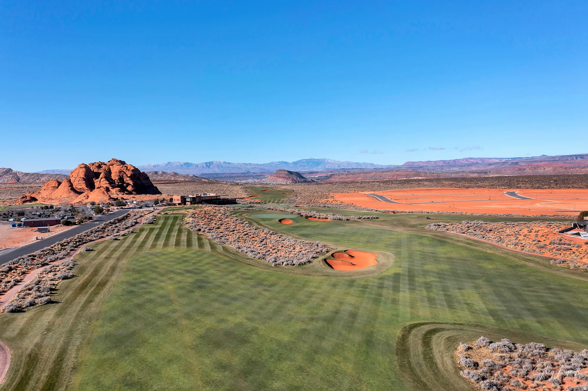 Expansive golf course landscape featuring meticulously manicured greens, natural desert vegetation, and striking red rock formations