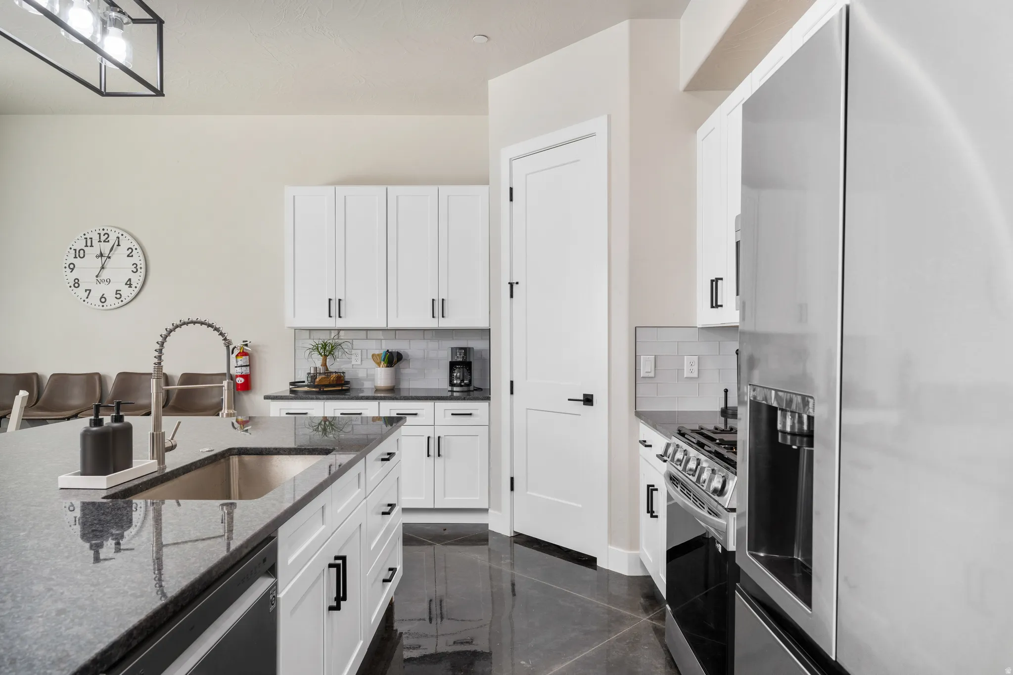 Contemporary kitchen featuring white cabinetry with matte black hardware, stainless steel appliances, a deep basin sink with a gooseneck faucet, and dark granite countertops