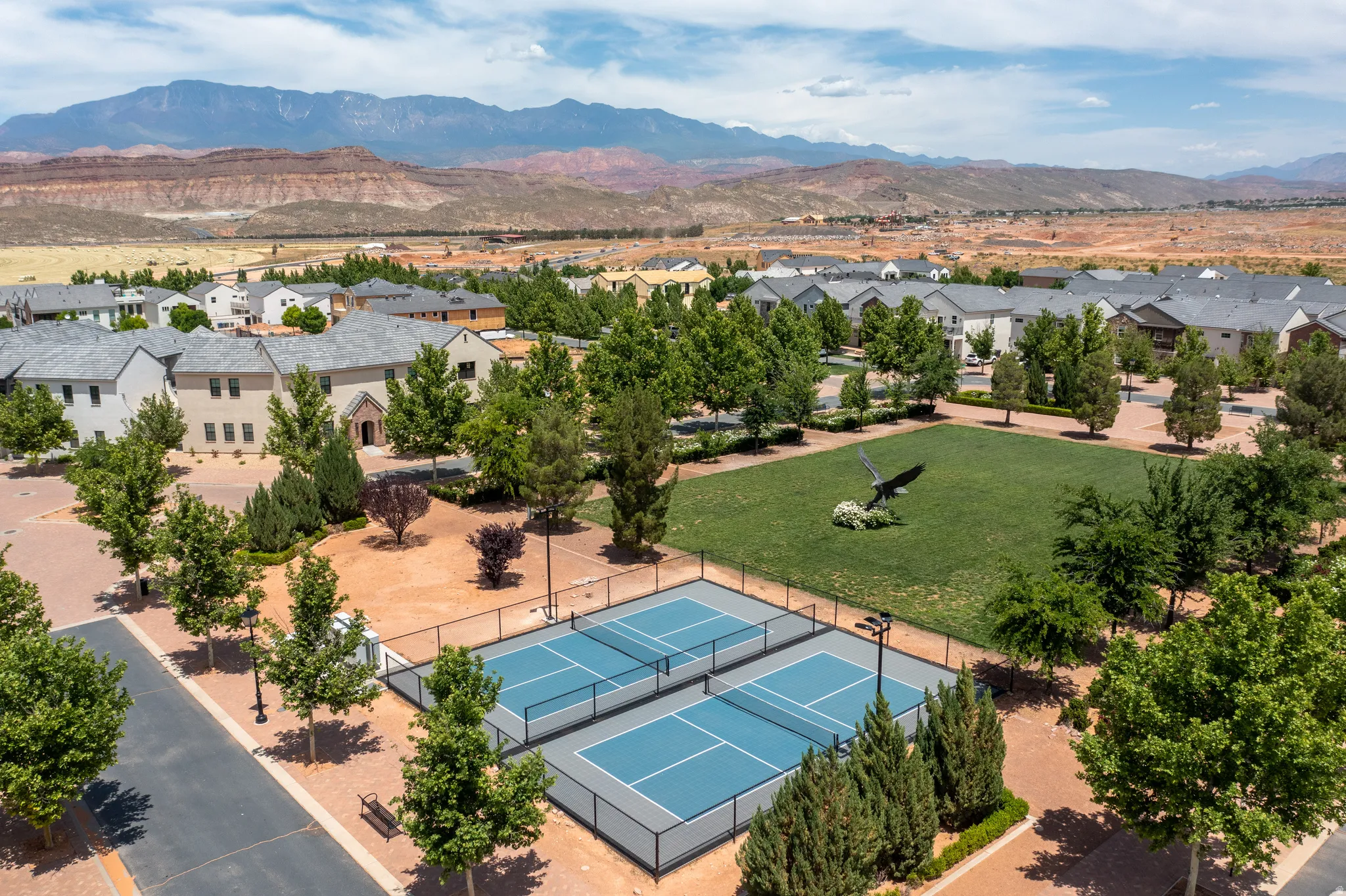 Community green space with two blue pickleball courts, manicured lawn, and mature landscaping