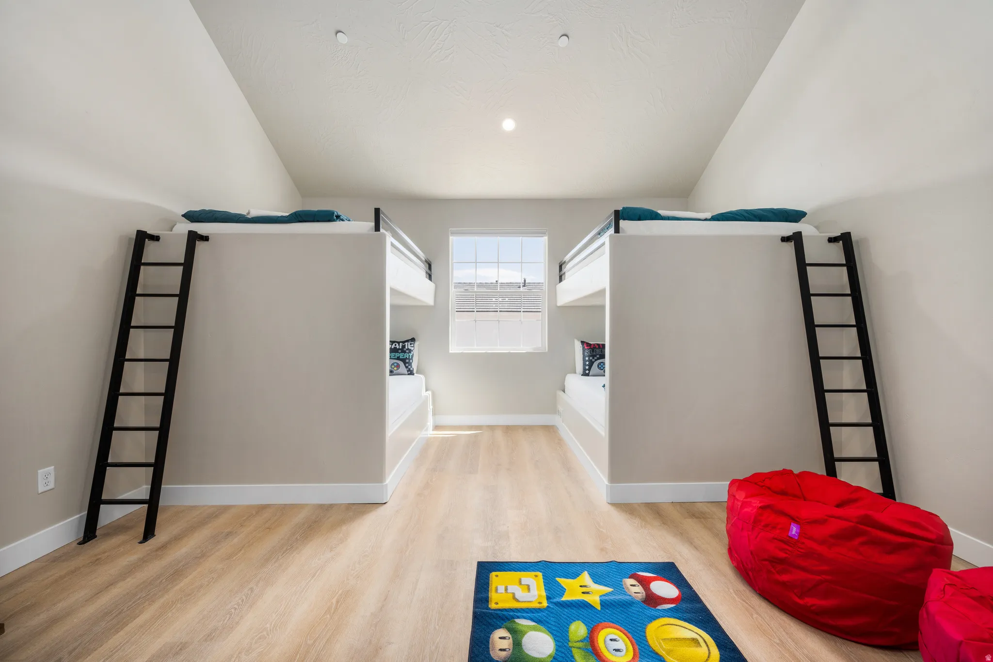 Room featuring built-in bunk beds with black ladders, light wood-finish flooring, and a single window