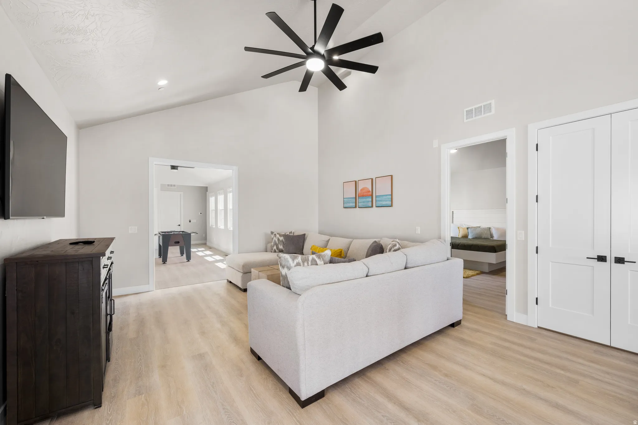 Bright living area with vaulted ceilings, a large black ceiling fan, and light wood-finish flooring