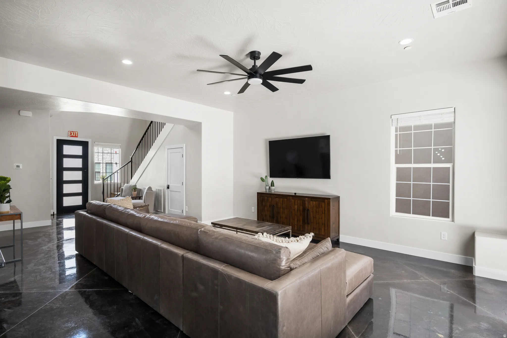 Spacious living area featuring polished concrete flooring, a contemporary ceiling fan, and recessed lighting