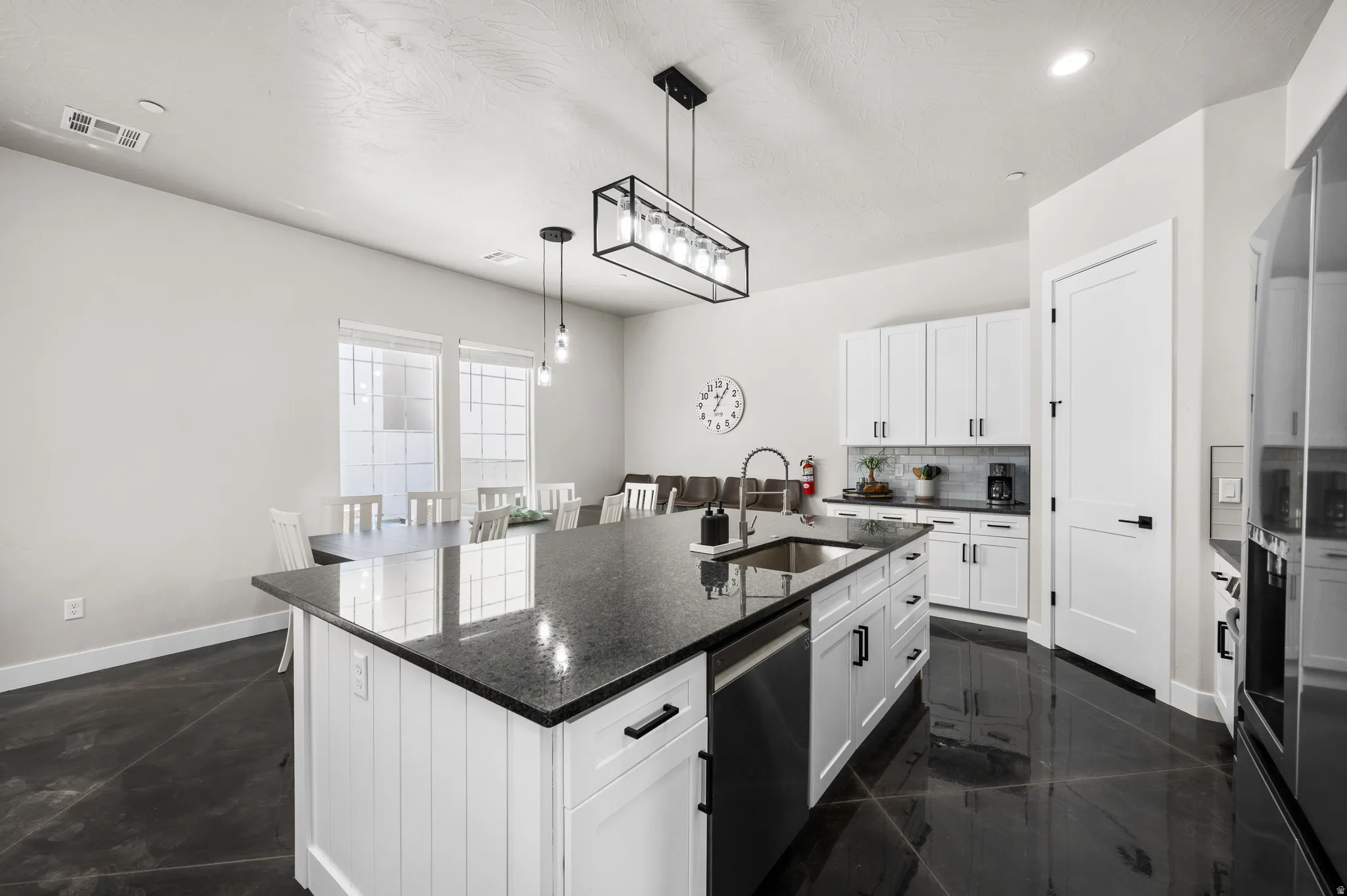 Open-concept kitchen featuring a large island with a sink, white cabinetry, dark countertops, and stainless steel appliances