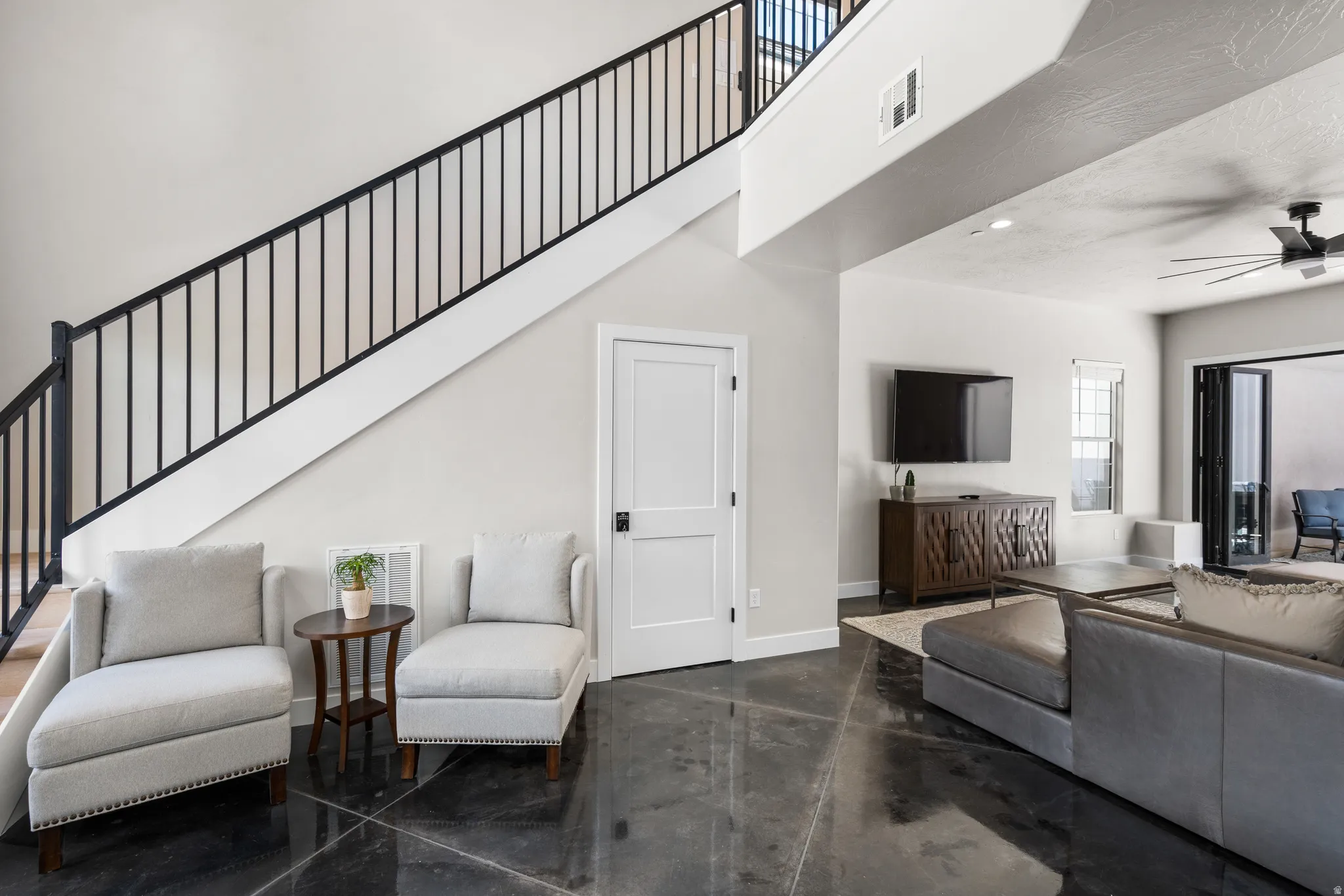 Open-concept living space featuring a modern staircase with dark metal railings, polished dark flooring, and a ceiling fan