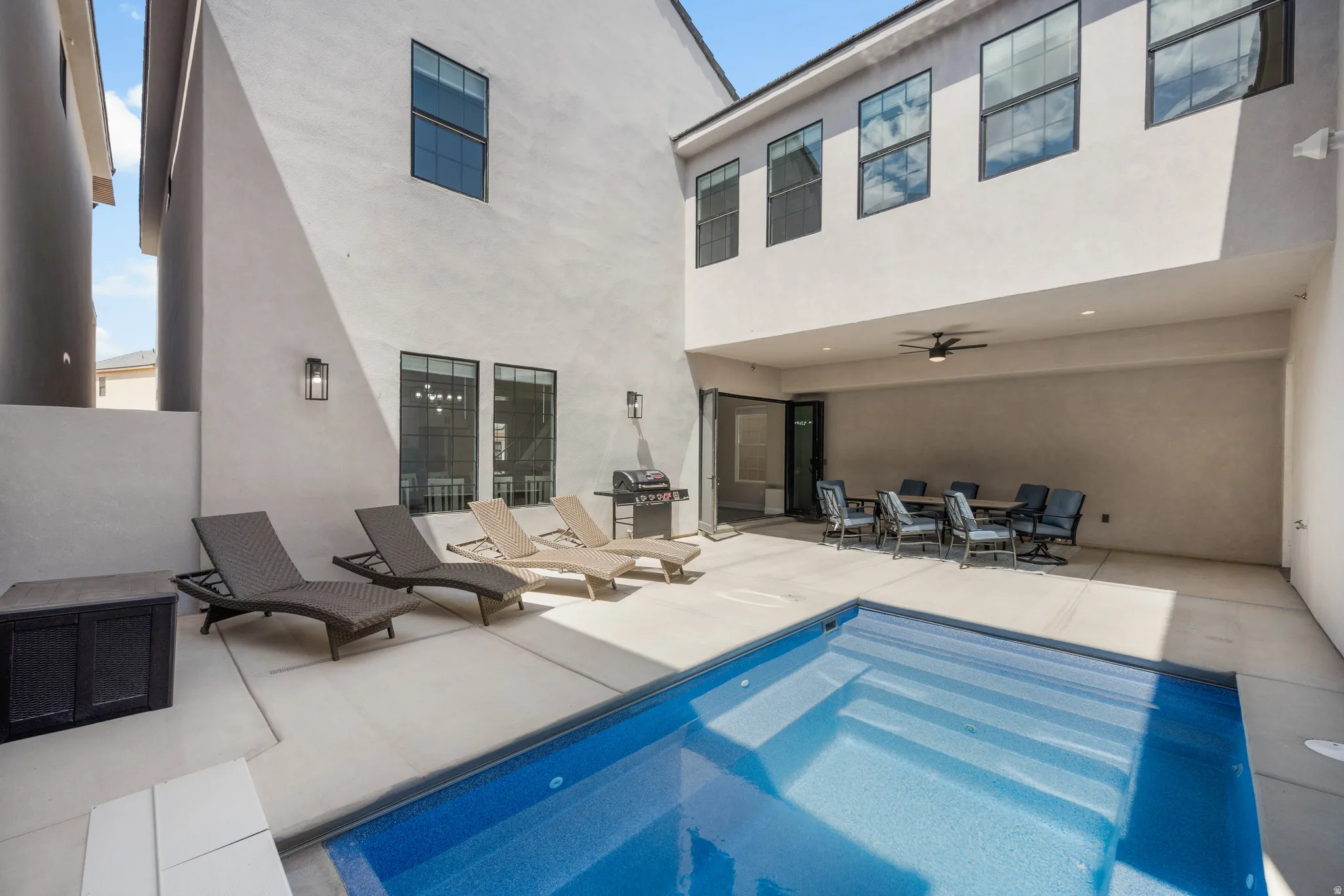 Private courtyard featuring a rectangular pool with integrated steps, a covered patio with a ceiling fan, and large format windows