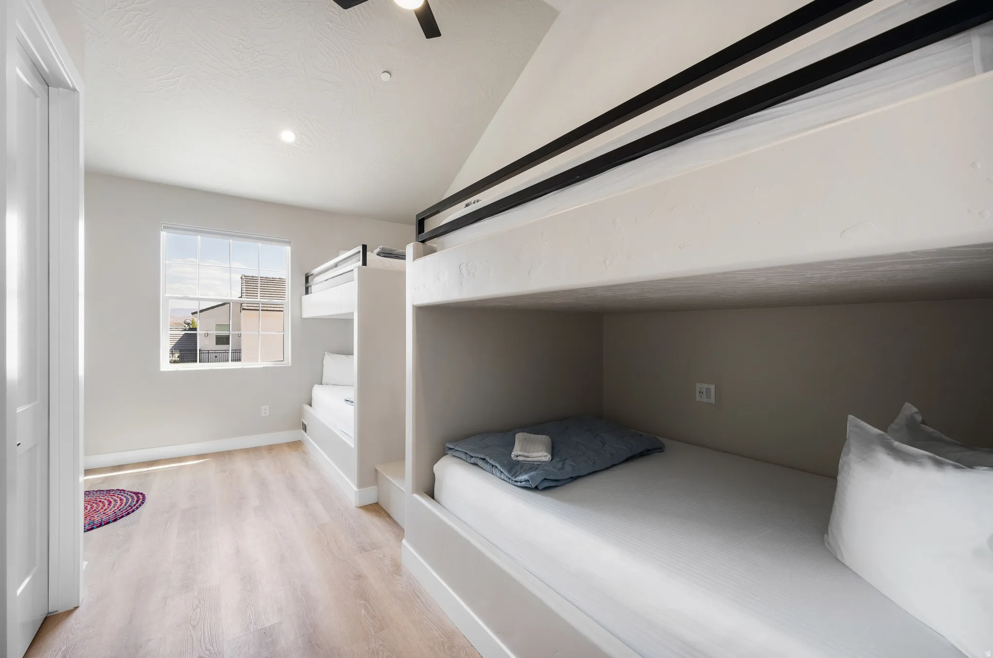 Room featuring built-in bunk beds with black metal railings, wood-finish flooring, a window with exterior views, and a ceiling fan